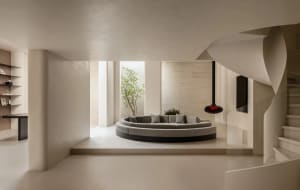 A modern living room with a circular couch, a potted plant, and a vase, set against a backdrop of white walls and well-lit for a comfortable atmosphere