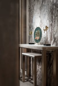 A modern dining space with a marble countertop, a marble-textured wall, a table, a vase, and a chair, lit by soft warm light