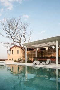 A backyard living space with a pool, patio, and gazebo, surrounded by a wooden fence and featuring natural materials and warm sunlight