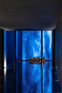 Blue-lit living room with a blue-tinted glass door, blue walls, and a couch in a modern and contemporary space