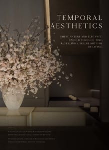 A white vase filled with pink flowers sits on a table in a room with a couch in the background
