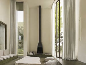 Cozy modern living space with a stone fireplace, a large window, and natural materials, featuring a bed, couch, chair, and books