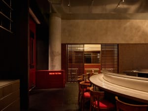 Cozy restaurant interior with a wooden bar, red chairs, and dim lighting, featuring a mix of wood and metal elements
