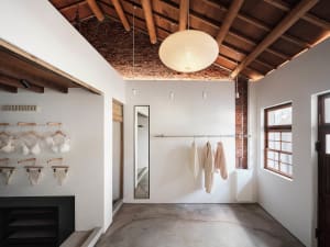 Dimly lit clothing store with white floor, brick wall, and hanging clothes, a mirror, and a cozy atmosphere