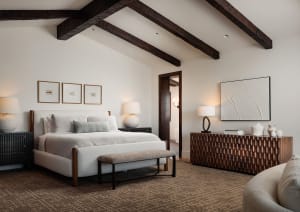 Modern rustic bedroom with white walls, exposed dark wooden ceiling beams, upholstered bed with neutral linens, textured wooden console, and herringbone carpet.