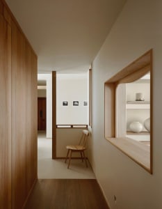 Modern minimalist hallway featuring light oak wood paneling, a built-in curved display niche with white ceramic vases, and a wooden chair against a white wall with small framed photographs.