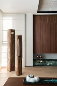 Modern minimalist entryway featuring two large weathered wood sculptures, a walnut wood wall cabinet, green marble ledge with bronze figurines, and a white horse sculpture on a dark console.
