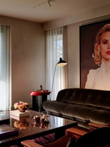 Modern living room with dark green tufted velvet sofa, glossy patterned lacquered coffee table, red side table, black floor lamp, and large Marilyn Monroe portrait artwork.