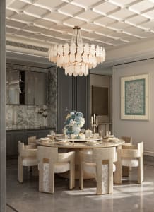 Luxurious dining room featuring a large round marble-top table surrounded by six mother-of-pearl inlaid dining chairs, a large white capiz shell chandelier, marble floor, and grey cabinetry with a floral centerpiece.