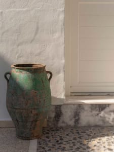 Large antique green ceramic urn with two handles placed on a terrazzo floor next to a white textured wall and marble base.