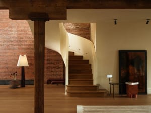 View of a dramatic curved wooden staircase with exposed dark wooden beams and red brick walls in a modern industrial loft interior.