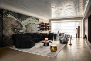 Modern luxury living room featuring a large dramatic green marble wall, black velvet modular sofa, patterned accent chairs, round black coffee table, and metallic ceiling.