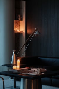 Modern living room featuring a black leather sofa, dark wood paneling, warm candlelight on a black coffee table, and a sculptural floor lamp creating a moody nighttime atmosphere.