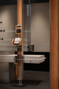Modern minimalist reception kiosk made of oak wood and concrete with brochure holder and digital display screen.
