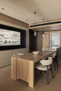Modern dining area featuring a solid oak island table, boucle upholstered chairs, black pendant lights, and a large monochrome photograph of horses on a wood-paneled wall.