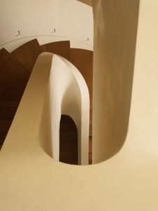 View looking down a modern curved staircase featuring smooth off-white plaster walls and balustrade paired with dark oak wooden treads and recessed ceiling lighting.