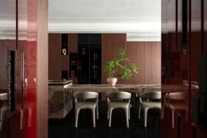 Modern luxury dining room featuring a large marble dining table, four beige upholstered chairs, a bonsai tree centerpiece, rich walnut wood cabinetry, and glossy red lacquer panels.