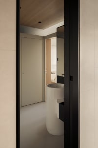 Modern minimalist bathroom featuring a cylindrical white porcelain sink with black floating vanity, viewed through a dark door frame with wood ceiling and neutral walls.