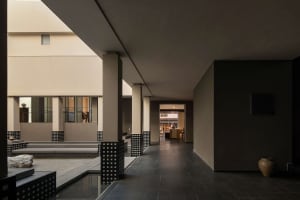Modern minimalist courtyard featuring a shallow water channel, concrete pillars with black lattice bases, built-in stone seating, and a large ceramic jar against a dark wall.