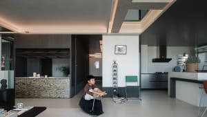 Modern open-plan living and kitchen area with dark wood grain feature wall, concrete ceiling details, and a child playing on a rocking horse.
