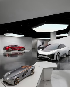 Three futuristic concept cars in red, white, and silver displayed on a glossy floor in a modern exhibition space with black ceiling and white geometric walls.