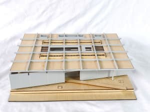 Architectural scale model of a modern house featuring a white grid facade, wooden structural elements, and an elevated wooden deck base.