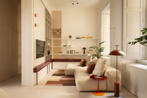 Modern minimalist living room featuring a large cream modular sofa, terracotta red accents, built-in white shelving, and a colorful striped rug.