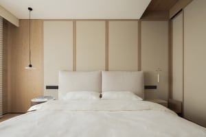 Modern minimalist bedroom featuring a large bed with a textured beige fabric headboard, white bedding, light oak wood paneling on the wall, and matching floating nightstands with pendant lights.