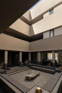Modern sunken courtyard with built-in concrete seating, large natural boulder centerpiece, and multi-level architectural walls under an open sky.