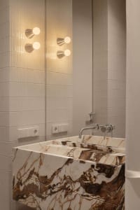 Modern bathroom featuring a thick Calacatta marble floating vanity with dramatic brown veining, paired with vertically ribbed white wall tiles and contemporary brushed-nickel wall sconces and faucet.