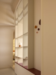 Modern arched built-in shelving unit in off-white with terracotta-colored base and decorative hooks, featuring a spherical table lamp on one shelf.