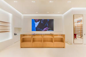 Modern minimalist retail store interior with white walls, glossy floor, recessed lighting, and a central light oak display counter with glass top.
