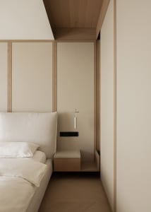 Modern minimalist bedroom corner showing a beige upholstered bed with white linens, a wall-mounted oak floating nightstand, and a slim white pendant light hanging from a wood-paneled ceiling.