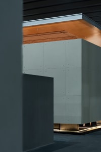 Modern architectural interior featuring a large floating concrete cabinet with visible bolt details, warm wood ceiling with linear slats, and dramatic indirect lighting at the base.