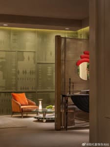 Modern living room featuring sage green textured walls, a burnt orange velvet armchair, glass coffee table, and a bronze mesh room divider with red circular mirror.