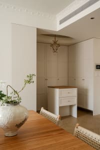 Elegant dining area featuring a wooden console table, woven rattan dining chairs, a large ceramic vase with greenery, and tall cream-colored built-in cabinetry with crown molding.