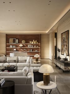 Modern luxury living room with a large white sectional sofa, illuminated walnut built-in shelving wall, marble table lamps, and polished stone flooring.