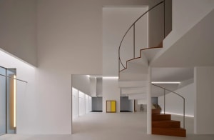 View looking down a modern minimalist white staircase with curved wooden handrail, warm wood treads, and a long linear skylight above.