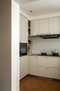 Modern minimalist L-shaped kitchen featuring matte cream cabinetry, black countertop, built-in oven, gas cooktop, and herringbone wood flooring.