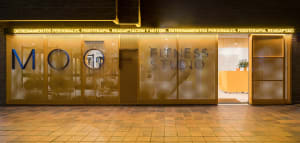 Night view of a modern fitness studio entrance featuring a glowing golden perforated metal facade with circular windows and illuminated signage.