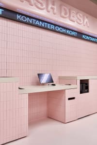 Modern cash desk covered in glossy pink square tiles with a built-in monitor and digital signage reading 'KONTANTER OCH KORT' against a matching pink tiled wall.