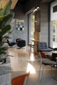 Modern cafe interior featuring ribbed wood paneling, black velvet swivel armchairs, grey corduroy lounge chair, metallic bar stools, and large windows with natural light.
