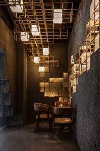Modern restaurant dining nook featuring textured plaster walls, leather upholstered chairs, and a striking golden grid light installation hanging from the ceiling.