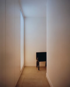 Narrow minimalist hallway with light oak herringbone floor, tall built-in cabinet on the left, and a black modern console table at the end under soft ambient lighting.