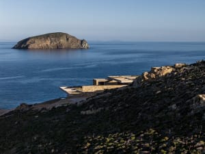 Modern stone and concrete cliffside villa overlooking the blue Mediterranean sea and a rocky island at golden hour.