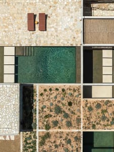 Top-down aerial photograph of a modern Mediterranean courtyard with a rectangular turquoise swimming pool, two wooden lounge chairs, pebble stone paving, and geometric drought-resistant garden beds.