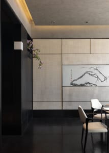 Modern Chinese-style dining room featuring dark wood furniture, cream textured wall panels, a large ink wash painting of a mountain and tree branch, and a hanging pink flowering branch.