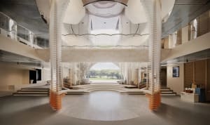 Modern double-height atrium lobby featuring tall white biomorphic columns with terracotta bases, polished terrazzo flooring, curved steps, and a large arched opening revealing green landscape beyond.