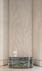 Modern luxury lobby featuring a green serpentine marble reception desk beneath a large abstract beige wall mural with flowing organic lines, illuminated by a small crystal table lamp.