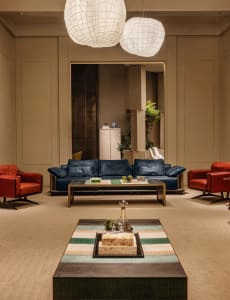 Modern luxury living room featuring a deep navy blue leather sofa, two vibrant red leather swivel armchairs, a low metallic coffee table, and a foreground striped leather ottoman with marble decor, all beneath large white woven spherical pendant lamps.